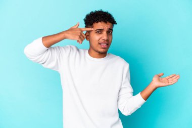 Genç Afro-Amerikalı kıvırcık adam mavi salonda izole edilmiş ve elinde bir ürün var..