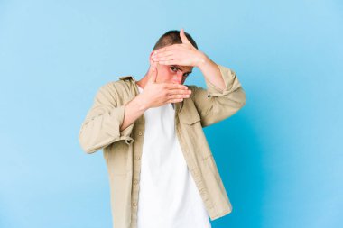 Genç, beyaz, yakışıklı bir adam kameraya parmaklarıyla göz kırpıyor, utanarak yüzünü kapatıyor..