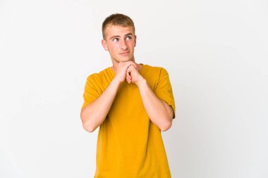 Beyaz tenli yakışıklı adam ellerini çenesinin altında tutuyor ve mutlu bir şekilde yan tarafa bakıyor..