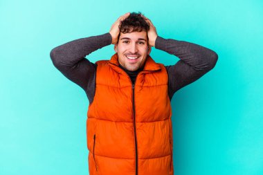 Genç beyaz adam mavi arka planda izole edilmiş bağırıyor, çok heyecanlı, tutkulu, bir şeyden memnun..