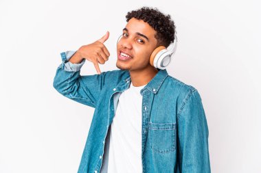 Genç Afro-Amerikalı kıvırcık adam izole edilmiş kulaklıkla müzik dinliyor parmaklarıyla bir cep telefonu hareketi gösteriyor..