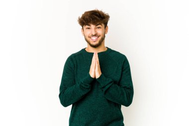 Beyaz arka plandaki genç Arap adam, el ele tutuşup, ağzının kenarında dua ediyor, kendinden emin..