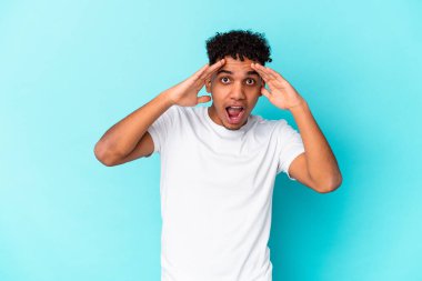 Genç Afro-Amerikalı kıvırcık adam mavi üzerine izole edilmiş. Hoş bir sürpriz alıyor, heyecanlı ve el kaldırıyor..