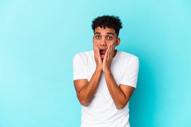 Genç Afro-Amerikan kıvırcık adamı mavi renkte izole edilmiş ağzı ellerle kaplanmış, yeni bir şey keşfetmek için sabırsızlanıyor..