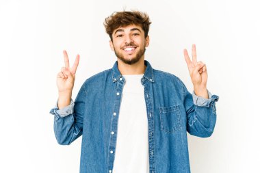 Beyaz arka planda genç bir Arap zafer işareti gösteriyor ve gülümsüyor..