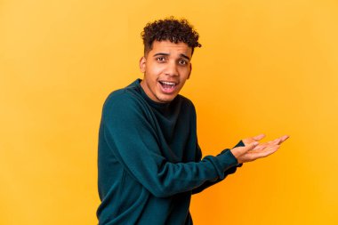 Genç Afro-Amerikalı kıvırcık adam, mor üzerine izole edilmiş. Elinde palmiye ağacında bir kopya alanı var..