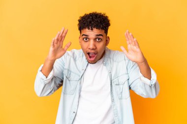 Genç Afro-Amerikalı kıvırcık adam, mor üzerine izole edilmiş. Hoş bir sürpriz alıyor, heyecanlı ve el kaldırıyor..