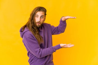 Uzun saçlı genç adam şok olmuş ve hayret içinde. Ellerinin arasında bir kopya alanı tutuyor..