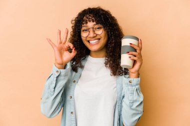 Afro-Amerikan Afro kadın elinde hazır kahveyle neşeli ve kendinden emin bir şekilde iyi bir jest yapıyor..