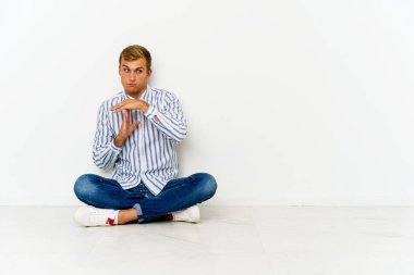 Genç, beyaz bir adam yerde oturuyor ve bir jest yapıyor..