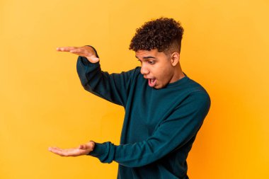 Genç Afro-Amerikan kıvırcık adamı, mor renkte izole edilmiş, şok olmuş ve hayret içinde, elleri arasında bir kopya alanı tutuyor..