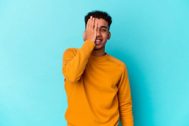 Genç Afro-Amerikalı kıvırcık adam mavi üzerine izole edilmiş. Yüzünün yarısını palmiye ile kaplayarak eğleniyor..