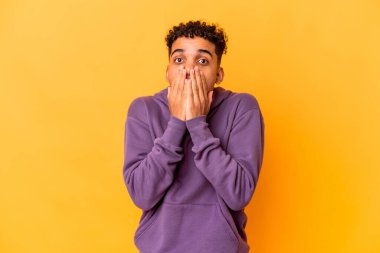 Genç Afro-Amerikan kıvırcık adamı mor renkte izole edilmiş, ağzı ellerle kaplanmış, yeni bir şey keşfetmek için sabırsızlanıyor..