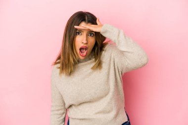 Pembe arka planda izole edilmiş genç Hintli kadın uzaklara bakıyor ve elini alnına koyuyor..