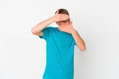 Genç, beyaz, yakışıklı bir adam kameraya parmaklarıyla göz kırpıyor, utanarak yüzünü kapatıyor..