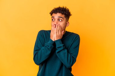 Genç Afro-Amerikalı kıvırcık adam mor düşünceli bir şekilde izole edilmiş. Ağzını eliyle kapatan bir fotokopi odasına bakıyor..