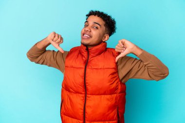 Genç Afro-Amerikan kıvırcık adamı mavi üzerine izole edilmiş gururlu ve kendinden emin hissediyor, örnek olarak.