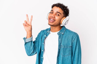 Genç Afro-Amerikan kıvırcık adamı, izole edilmiş, kulaklıklı, neşeli ve tasasız bir şekilde, parmaklarıyla barış sembolü gösteren bir müzik dinliyor..