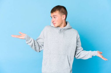 Kafası karışmış, genç, beyaz, yakışıklı bir adam. Kopyasını tutmak için omuz silkiyor..