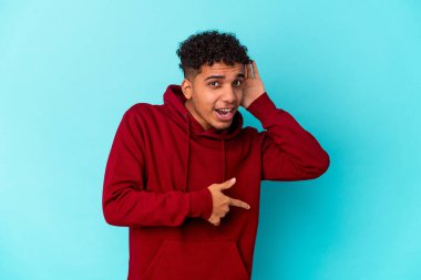 Genç Afro-Amerikalı kıvırcık adam mavi üzerine izole edilmiş bir şekilde bir dedikoduyu dinlemeye çalışıyor..