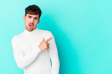 Mavi arka planda izole edilmiş genç beyaz adam yan tarafı işaret ediyor.