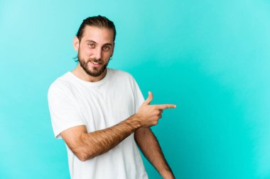 Uzun saçlı genç adam gülümsüyor ve işaret ediyor, boş alanda bir şeyler gösteriyor..