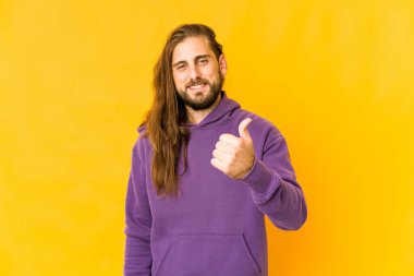 Uzun saçlı genç adam gülümsüyor ve başparmağını kaldırıyor.