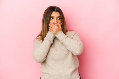 Genç Hintli bir kadın pembe arka planda izole edilmiş. Düşünceli bir şekilde fotokopi odasına bakıyor. Ağzını eliyle kapatıyor..