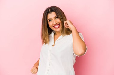 Pembe arka planda izole edilmiş genç Hintli kadın tasasız ve heyecanlı bir şekilde tezahürat yapıyor. Zafer konsepti.