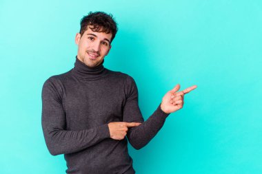 Mavi arka planda izole edilmiş genç beyaz adam işaret parmağıyla işaret ederek gülümsüyor..