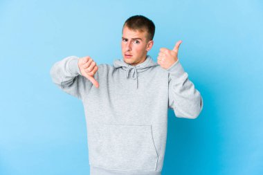 Kafkasyalı yakışıklı genç adam baş parmağını kaldırıyor ve baş parmak aşağı, zor seçim konsepti
