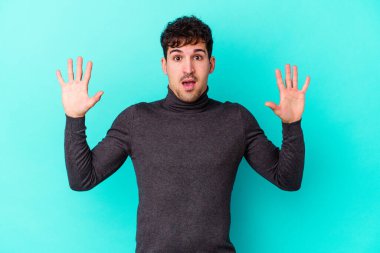 Kafkasyalı genç adam mavi arka planda izole edilmiş gökyüzüne haykırıyor, yukarı bakıyor, hayal kırıklığına uğramış..