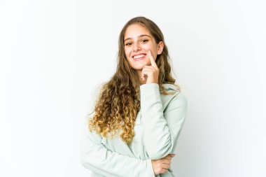 Genç beyaz kadın mutlu ve kendinden emin gülümsüyor, elleriyle çenesine dokunuyor..