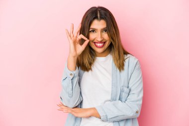 Pembe arka planda izole edilmiş genç Hintli kadın bir göz kırptı ve elleriyle iyi bir jest yaptı..