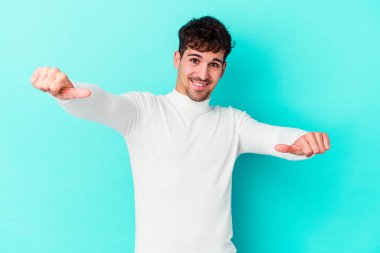 Kafkasyalı genç adam mavi arka planda izole edilmiş. Baş parmağını kaldırıyor, gülümsüyor ve kendinden emin..