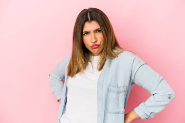 Pembe arka planda izole edilmiş genç Hintli kadın hoşnutsuzca kaşlarını çatmış, kollarını kavuşturmuş..