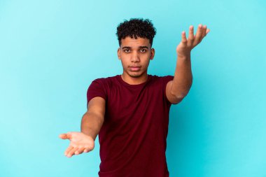 Genç Afro-Amerikan kıvırcık adamı mavi üzerine izole edilmiş kollarıyla ölçeği yapıyor, mutlu ve kendinden emin hissediyor..