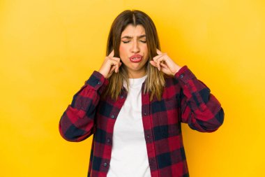 Sarı arka planda izole edilmiş genç bir Hintli kadın parmaklarıyla kulaklarını kapatıyor, gürültülü bir ortam yüzünden stresli ve çaresiz..