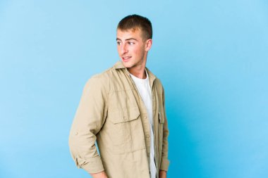 Genç beyaz yakışıklı adam gülümseyen, neşeli ve keyifli bir şekilde yana bakıyor..