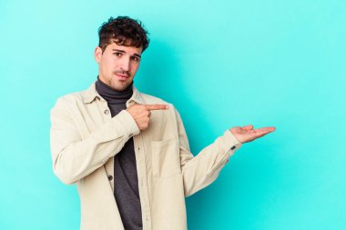 Kafkasyalı genç adam mavi arka planda izole edilmiş. Elinde palmiye ağacının bir kopyası olduğu için heyecanlı..