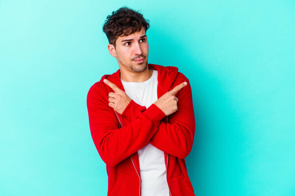 Молодой кавказский человек изолирован на синем фоне боком, пытается выбрать между двумя вариантами.