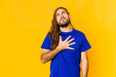 Uzun saçlı genç adam kahkahalarla gülüyor elini göğsüne koyuyor..