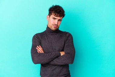 Kafkasyalı genç adam mavi arka planda izole edilmiş hoşnutsuzca kaşlarını çatmış, kollarını kavuşturmuş..