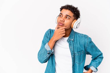 Genç Afro-Amerikalı kıvırcık adam kulaklıkla müzik dinleyip kuşkulu ve şüpheci bir ifadeyle yan gözle bakıyor..
