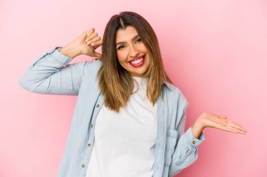 Pembe arka planda izole edilmiş genç Hintli kadın avuç içinde fotokopi alanı tutuyor, el üstünde tutuyor. Şaşırmış ve mutlu..