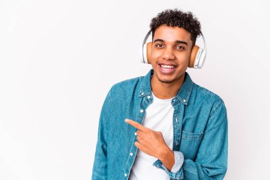 Genç Afro-Amerikan kıvırcık adamı, izole edilmiş, kulaklıklı müzik dinliyor, gülümsüyor ve boş alanda bir şeyler gösteriyor..