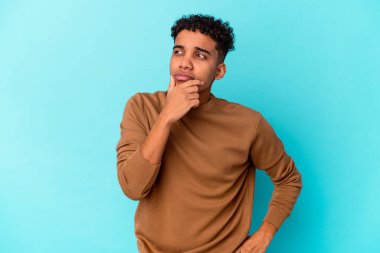 Genç Afro-Amerikan kıvırcık adamı şüpheli ve şüpheci bir ifadeyle mavi bir tarafa bakıyor..