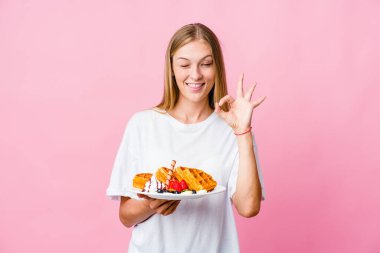 Genç Rus kadın waffle yerken yalnız bir göz kırpıyor ve elleriyle iyi bir jest yapıyor..