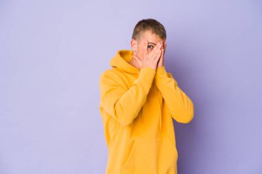 Genç, beyaz, yakışıklı bir adam parmaklarının arasından korkmuş ve gergin bir şekilde göz kırpıyor..