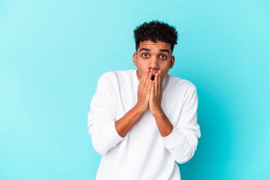 Genç Afro-Amerikan kıvırcık adamı mavi renkte izole edilmiş ağzı ellerle kaplanmış, yeni bir şey keşfetmek için sabırsızlanıyor..